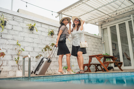 Two cheerful friends are happily posing by the sparkling pool during their sunny vacation getawayの写真素材