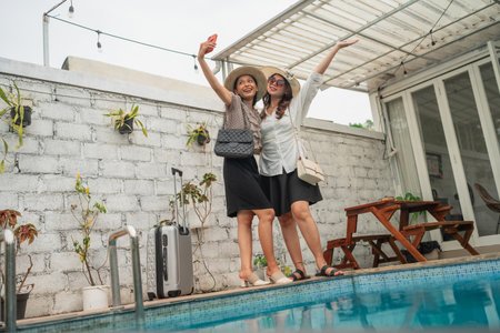Two close friends celebrate by the poolside, smiling and having fun in stylish summer hatsの写真素材