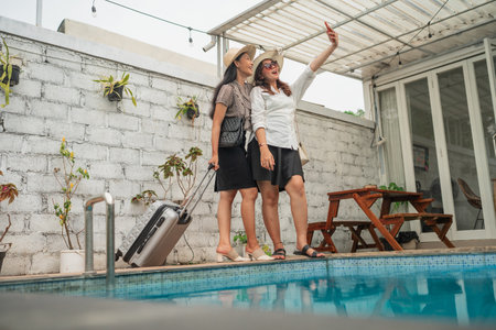 Two friends take a cheerful selfie by the pool, capturing their travel joy and friendshipの写真素材
