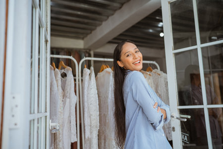 A smiling woman dressed in a light blue attire poses gracefully in front of elegant gownsの写真素材