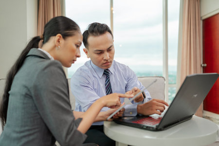 Professionals discuss strategies with a laptop and tablet in a modern office settingの写真素材
