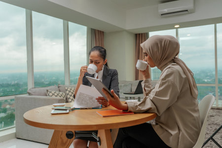 Two ambitious businesswomen share ideas over coffee in a stylish office, fostering collaborationの写真素材