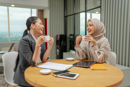 Two women are enjoying a joyful coffee break together in a contemporary workspace settingの写真素材