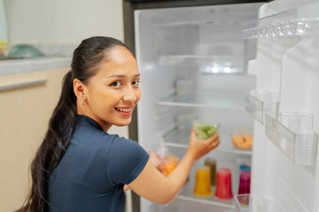 A woman smiles while arranging fresh fruits and drinks in her open refrigerator.の写真素材