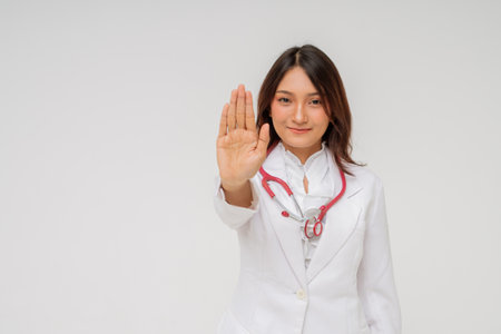 A female doctor is wearing a white coat and raises her hand to promote important health awarenessの写真素材