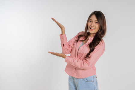 A cheerful woman joyfully showcasing something while smiling brightly on a plain backdropの写真素材