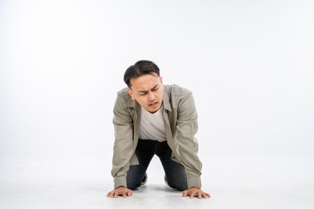 A young man is kneeling on the floor, showing signs of physical discomfort and struggleの写真素材