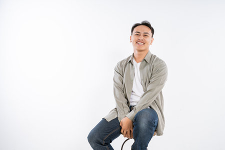 A cheerful and lively young man confidently poses on a stool, showcasing his unique style and charmの写真素材