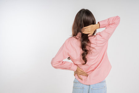 A woman who is experiencing discomfort in her back while sporting a casual and relaxed lookの写真素材