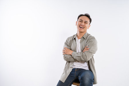 A cheerful young man smiles while sitting on a stool in a bright, inviting studioの写真素材