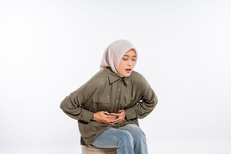 A woman experiences abdominal discomfort, sitting on a stool in a neutral setting.