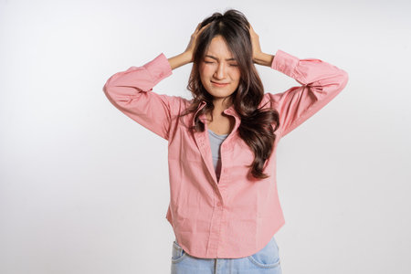 A young woman is visibly showing signs of significant stress while holding her head in despairの写真素材