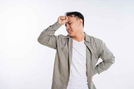 A young man is visibly expressing his feelings of frustration and discomfort as he holds his headの写真素材