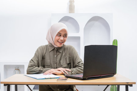 A warm and inviting office environment showcases a woman joyfully engaged with her laptop,