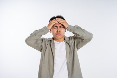 A young man visibly shows signs of stress as he holds his head in deep frustration and despairの写真素材