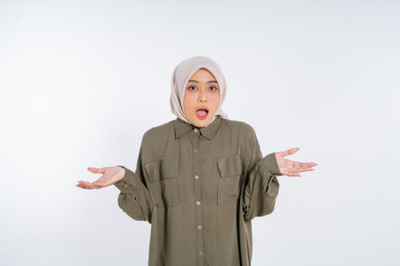 A young woman wearing a hijab expresses a mix of surprise and confusion with her hands raisedの写真素材