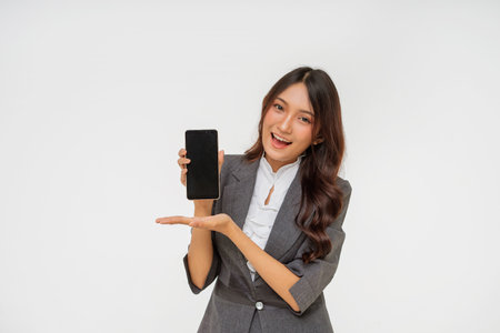 A confident and professional woman is proudly showcasing a modern smartphone in a studio settingの写真素材