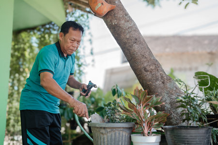 An elderly man is lovingly watering the vibrant plants in a wonderfully sunny garden settingの写真素材