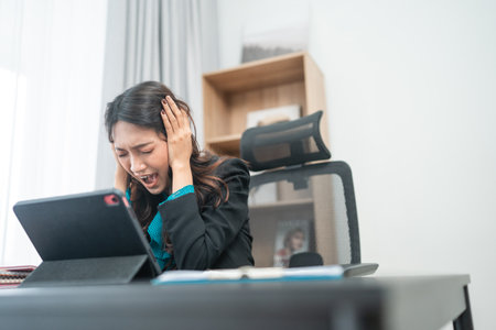 A stressed woman in a business suit struggles with her overwhelming workload at her deskの写真素材