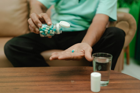 An individual is dispensing pills from a bottle, preparing to take them with waterの写真素材