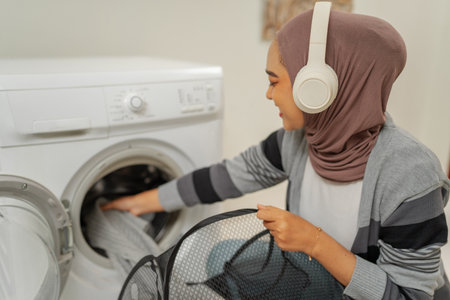 A cheerful and happy young woman enjoys doing her laundry while listening to soothing musicの写真素材