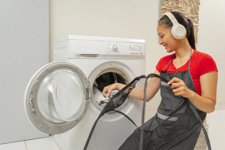 A cheerful woman is actively engaging with her laundry duties, all while enjoying musicの写真素材