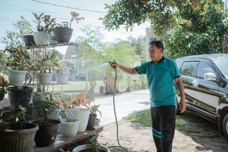 A man is carefully watering various plants in a vibrant garden full of diverse greeneryの写真素材