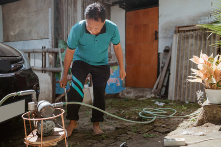 A man is actively and carefully working with a garden hose in a sunny outdoor area, barefoot