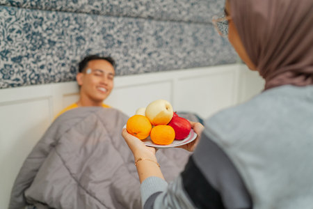 A woman brings fresh fruits to a man resting in bed, showing her care and supportの写真素材