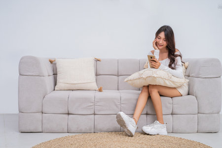 A young woman enjoys her time on the couch, engaged with her smartphone and cozy leisureの写真素材