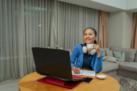 A positive and cheerful woman is enjoying her remote work while happily sipping a cup of coffee