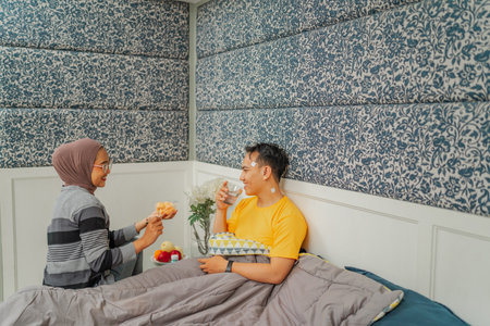 A couple enjoys breakfast in bed, sharing smiles and creating a warm, happy moment togetherの写真素材