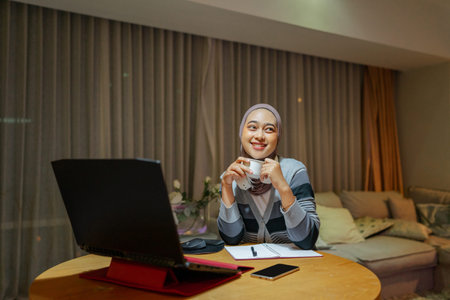 A happy woman enjoys her organized home office, using her laptop and sipping coffee