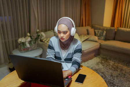 A young woman works online from home, wearing headphones to enhance her concentration