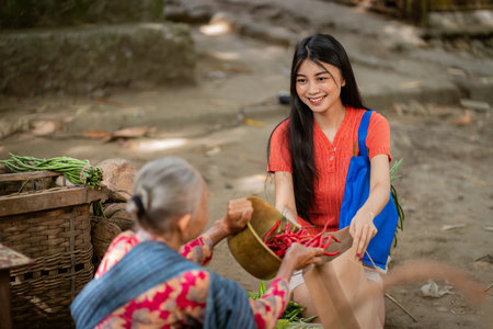 A young woman, with a smile of joy, happily receives freshly picked produce from an elder in a lively outdoor marketの写真素材