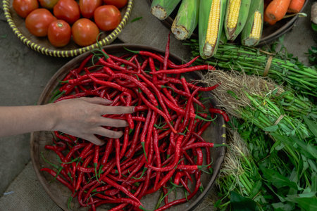 A vibrant market features a colorful display of fresh red chilies, juicy tomatoes, sweet corn, and...