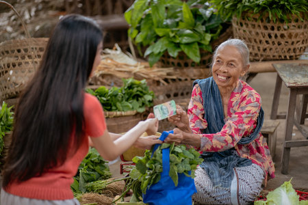 An elderly vendor happily engages with a young woman, showcasing the lively atmosphere of a bustling marketの写真素材