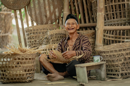 An elderly man, full of joy, skillfully weaves vibrant and colorful bamboo baskets in a peaceful, rustic rural settingの写真素材