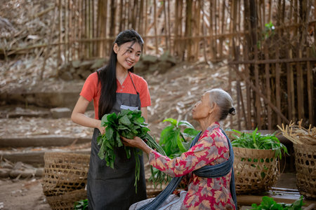 A young woman joyfully shares fresh greens with an elderly woman amidst the vibrant beauty of a scenic garden settingの写真素材