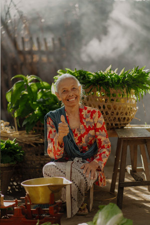 An elderly woman with a warm smile gives a thumbsup in a vibrant garden, embodying joy and traditionの写真素材