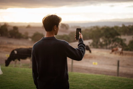 A person enjoying a sunset view while taking a photo in a rural setting.の写真素材