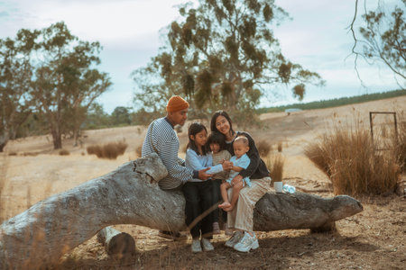 A loving family joyfully spends a beautiful day outdoors on a fallen treeの写真素材