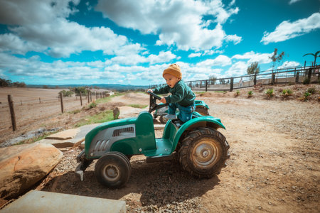 A joyful child drives a green toy tractor in a picturesque outdoor setting.の写真素材