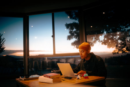 A young person is focused on a laptop, enjoying a beautiful sunset backdropの写真素材