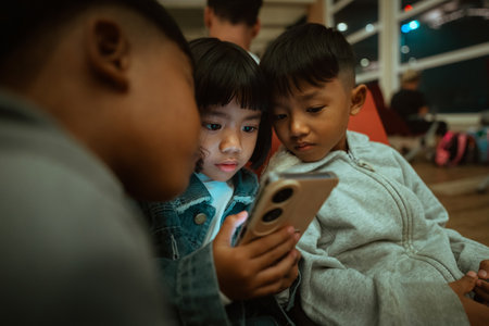 Three children gathered together, captivated by a smartphones screen.の写真素材
