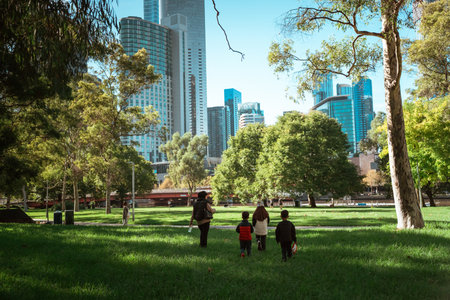 A family joyfully walking in a lush park with a vibrant city skyline backdropの写真素材