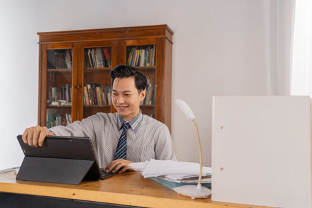 Asian man accountant organizes paperwork with tablet and smile, neat desk with invoices and ledgers,...