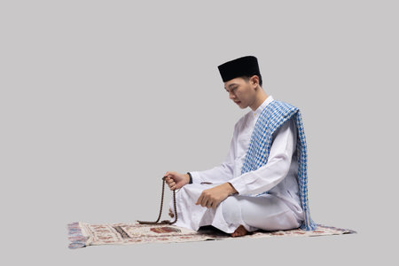 man seated on prayer mat holding beads, eyes closed in focused contemplation, neutral studioの写真素材