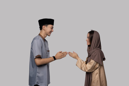 Colleagues sharing respectful professional greeting with open palms, mutual smiles, smart casual attire, headscarf and capの写真素材