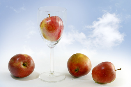 fresh red apples, one of them in a jar, symbol of apple juice, background bright blue sky with white cloudsの写真素材